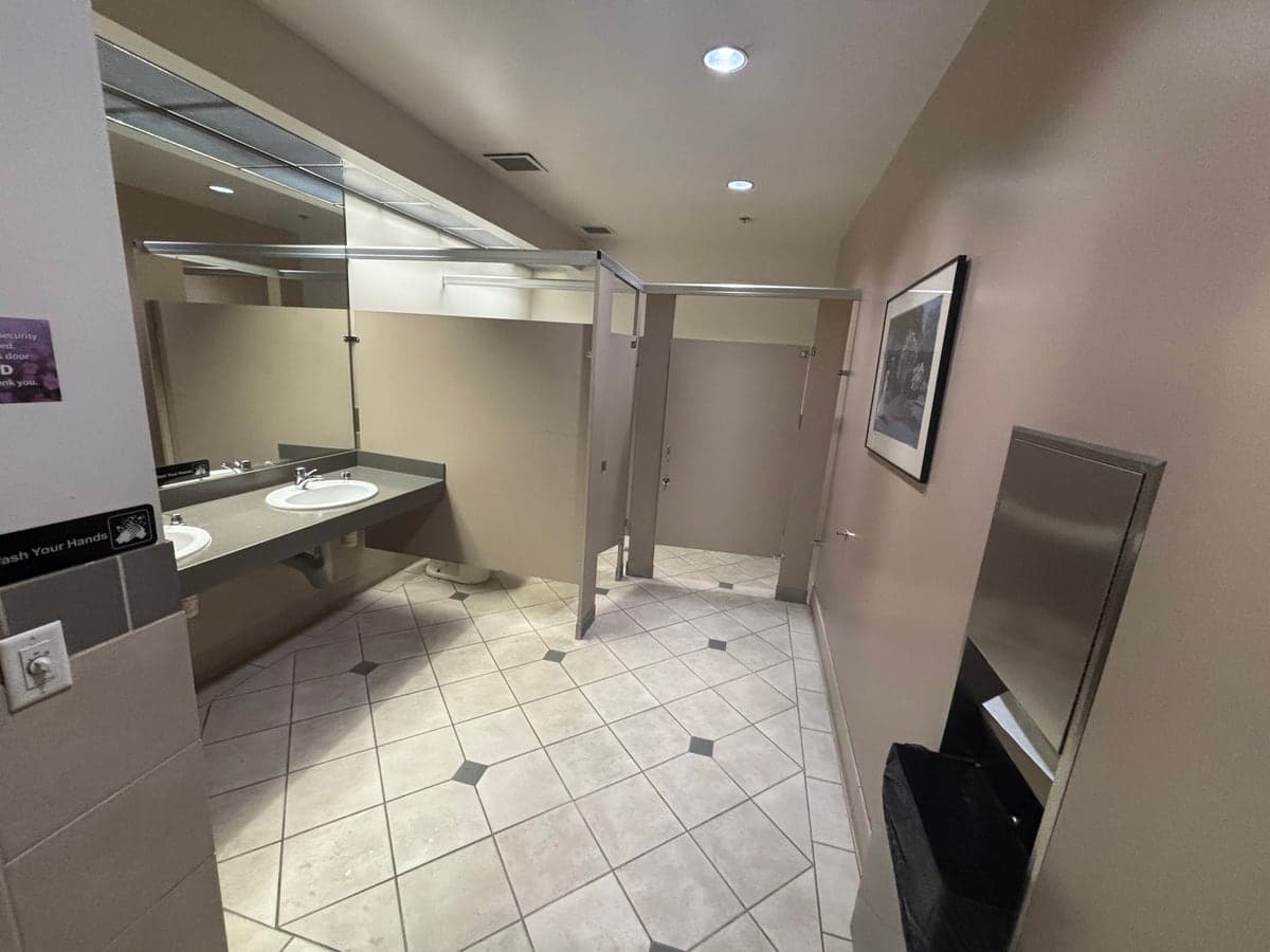 Clean common-area restroom with tiled floor, sinks, and stalls at a commercial office building serviced by Guardian