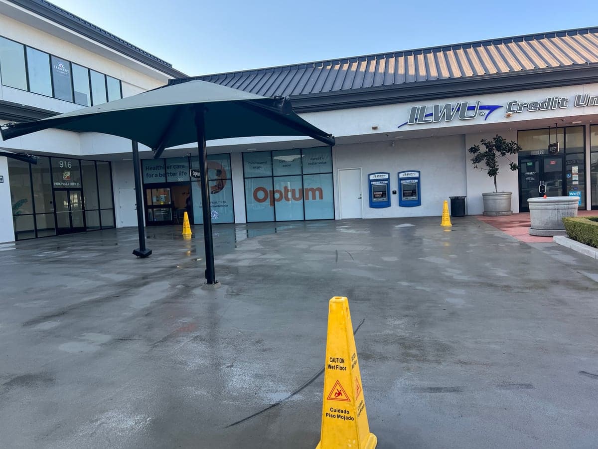 Freshly pressure-washed plaza courtyard with shade umbrellas in front of a clinic and credit union, wet-floor cones in place