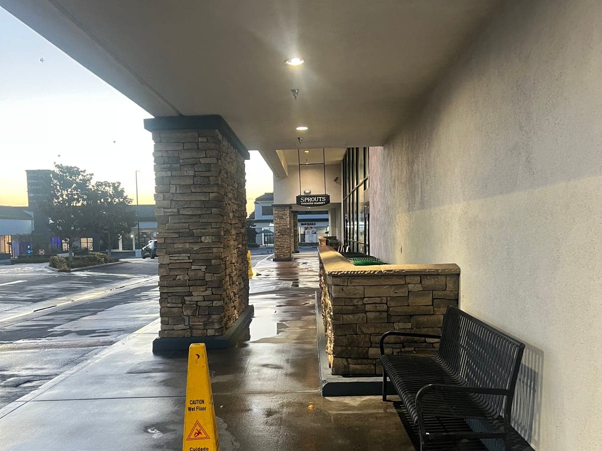 Covered retail walkway with stone columns and a bench after a scheduled pressure wash
